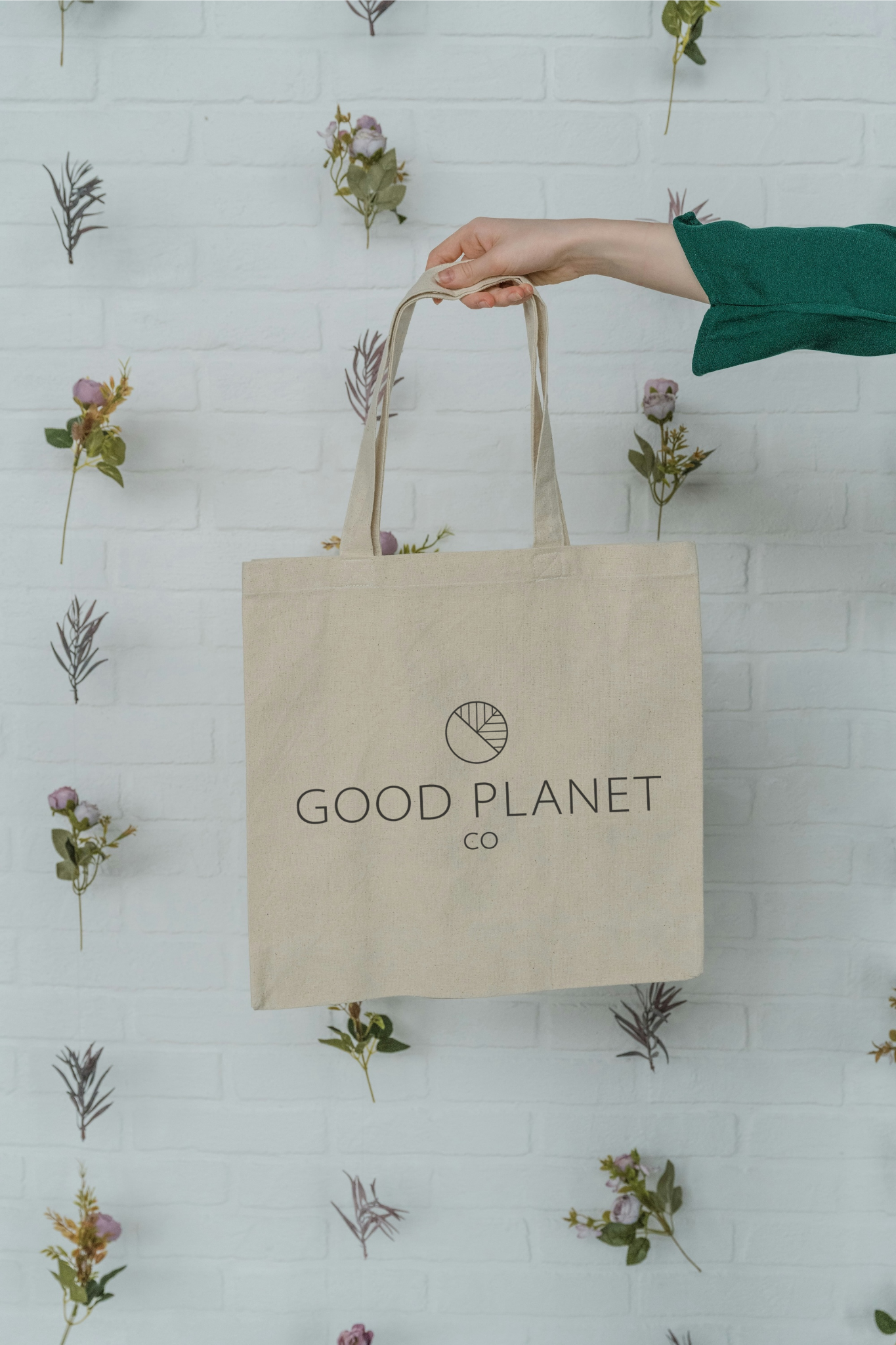 A hand holding out a organic cotton tote bag printed with the Good Planet Logo in the center of the bag.