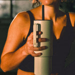 A woman sitting in a room after a workout sipping a beverage from a teal MiiR travel tumbler. 
